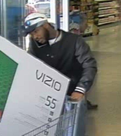black male pushing shopping cart with Vizio tv, talking on cell phone, with white and black cap with sunglasses on top