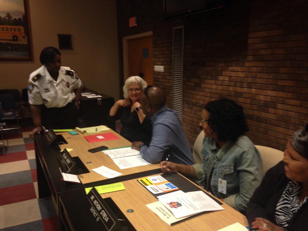 Four people sitting at a long table speaking with an officer