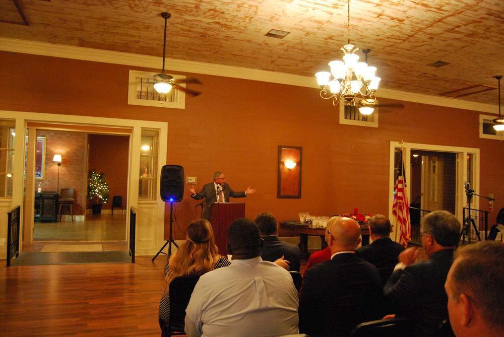 Man speaking at podium holding his hands out to the sides