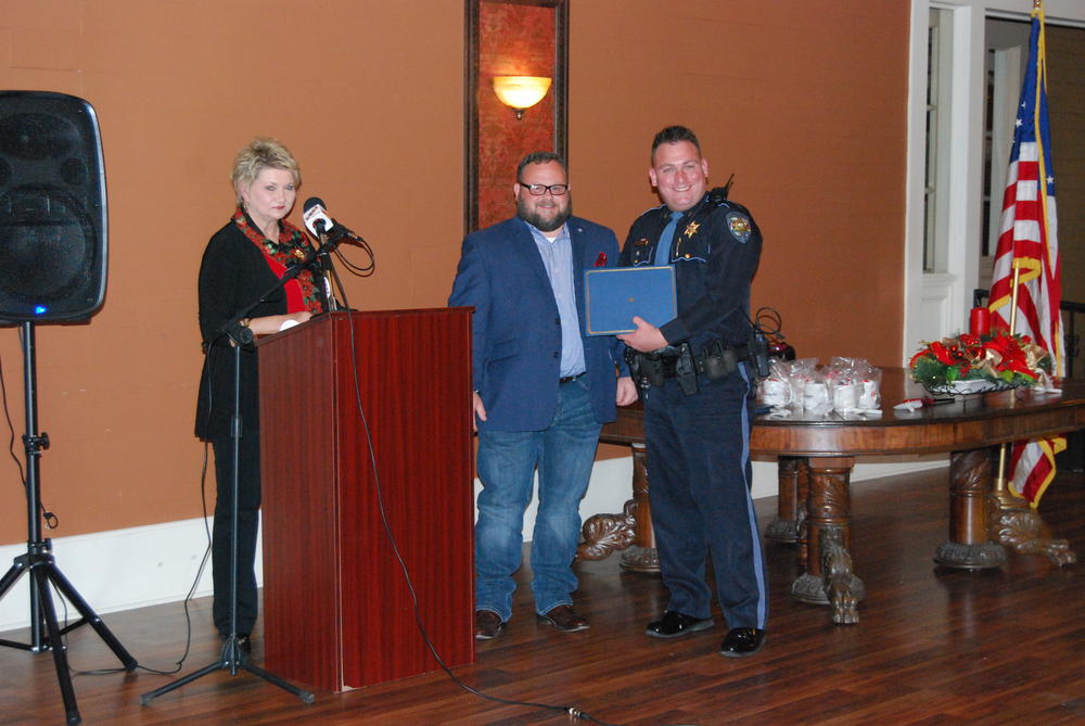 Two men standing beside a podium, one receiving an award, while woman stands at microphone