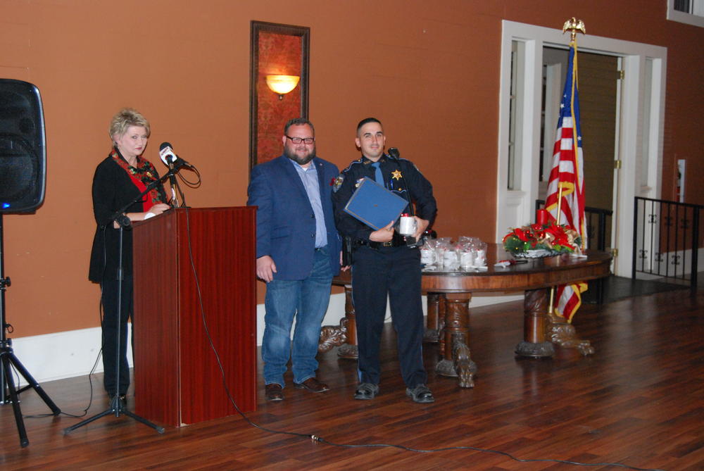 Woman at podium with two men standing next to podium, one receiving an award