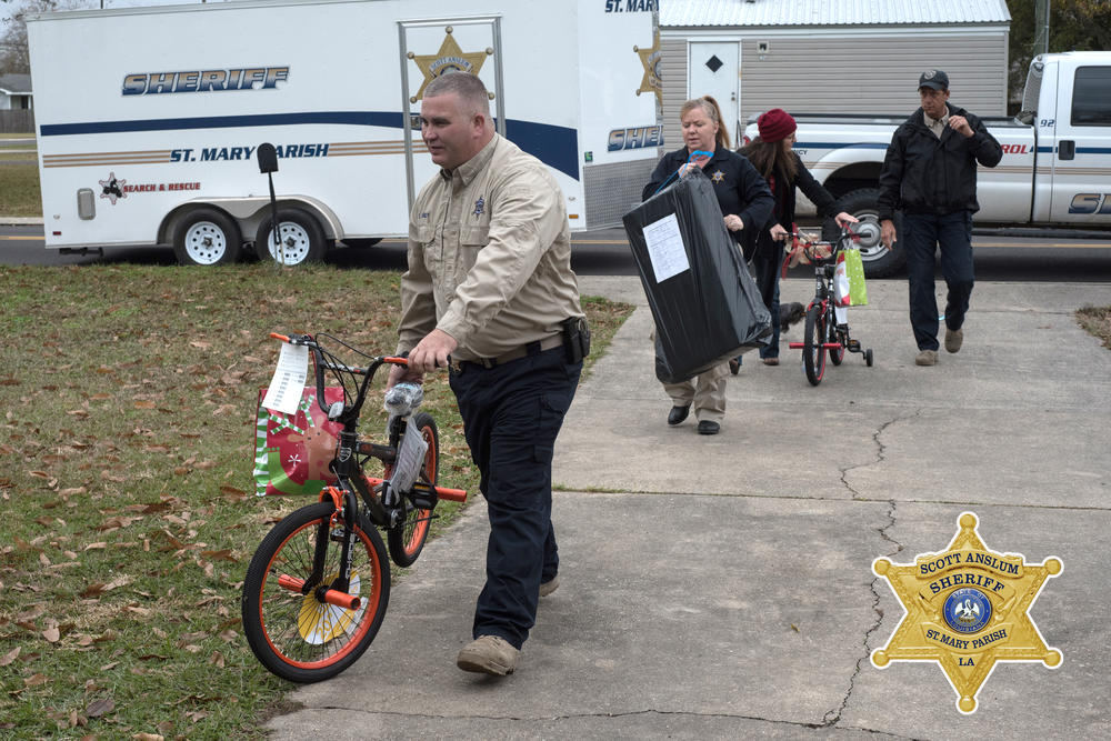 An line of officers walking gifts to a home. Some wrapped and a bicycle with a bow on it.