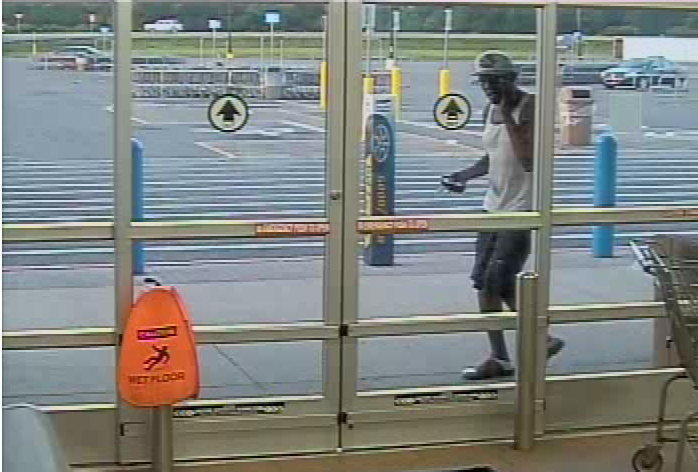 black male in white tank top and black shorts outside entrance doors, wearing white cap